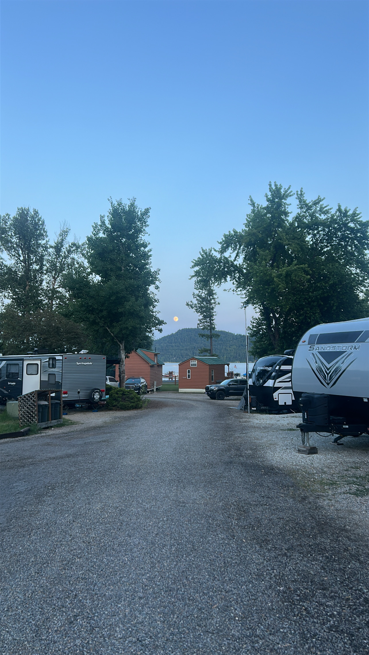 Evening view of RV sites with travel trailers and mountain backdrop under moonlight